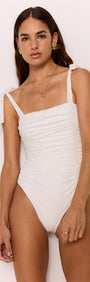 Model wearing white square-neck ruched broderie one-piece swimsuit with tie straps, showcasing stylish beachwear.