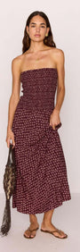 Model wearing a strapless burgundy floral print maxi dress with a ruched bodice and dropped hem, holding a handbag.