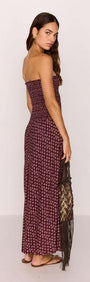 Model wearing a strapless burgundy floral maxi dress, showcasing a ruched bodice and dropped hem, holding a fringed bag.