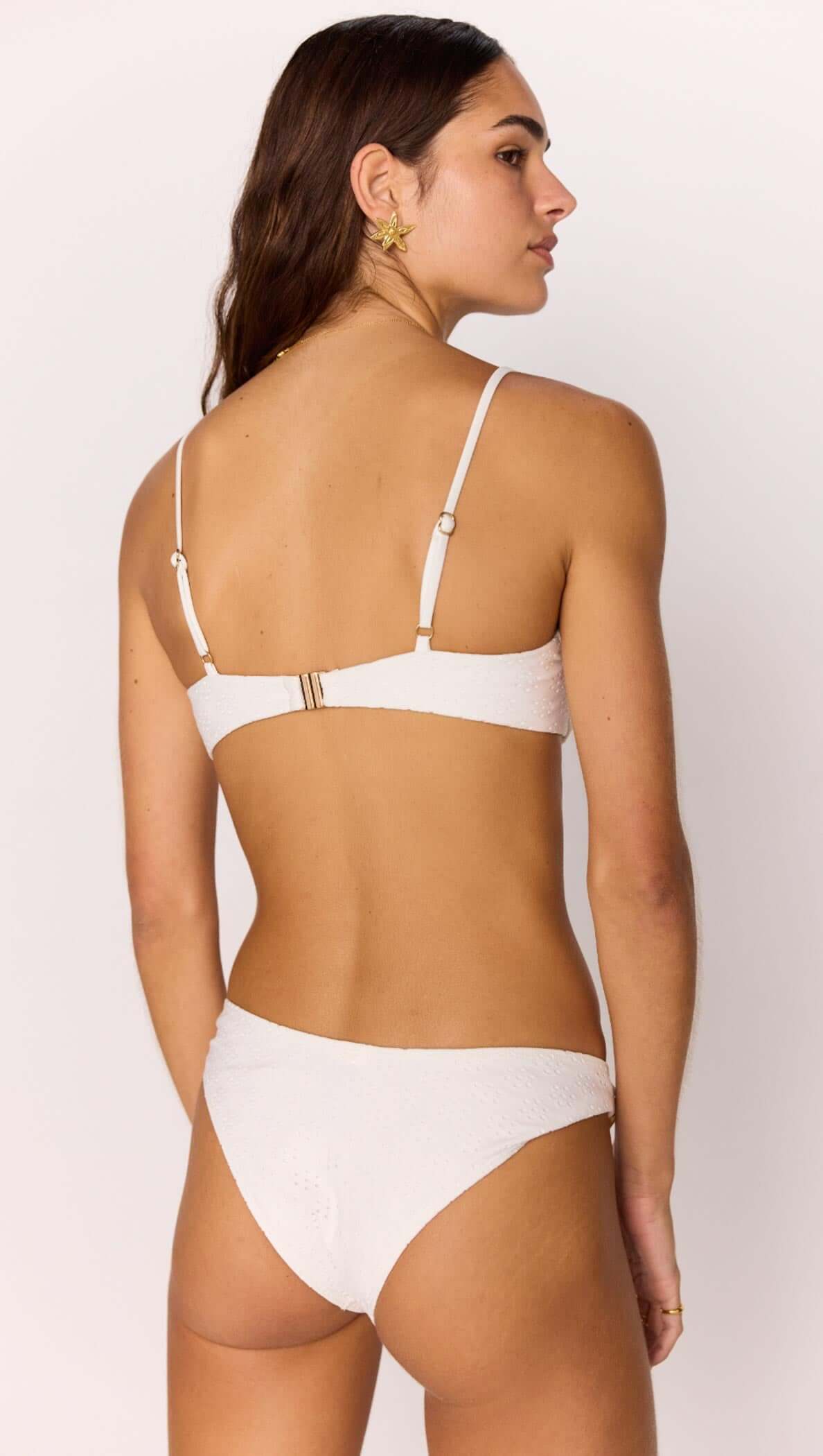 Back view of a woman wearing a white Broderie bikini pant with gold shell detail, showcasing stylish swimwear fashion.