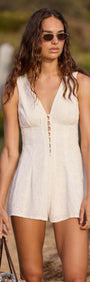 Model wearing a White Cotton Jacquard Button-Up Playsuit with deep V-neckline and flared shorts, captured on a beach.