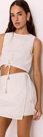 Model wearing a stylish Daphne White Wrap Mini Skirt with matching top, showcasing a relaxed summer look.