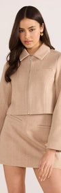 Model wearing a beige Audrey Herringbone mini skirt and matching jacket, showcasing a stylish high-rise fit and tailored lines.