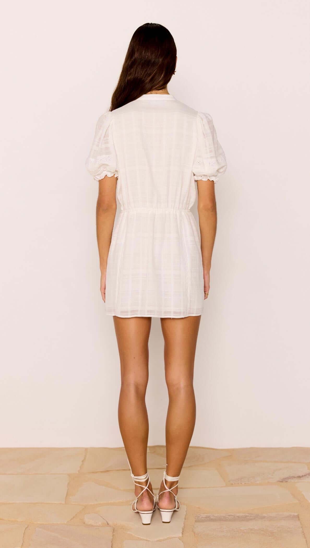 Model wearing the Lace Detail White Cotton Mini Dress, showcasing the back view with puff sleeves and elastic waist.