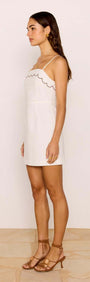 Side view of a woman wearing a Scallop Edge Cotton White Mini Dress by MINKPINK, perfect for summer outings.