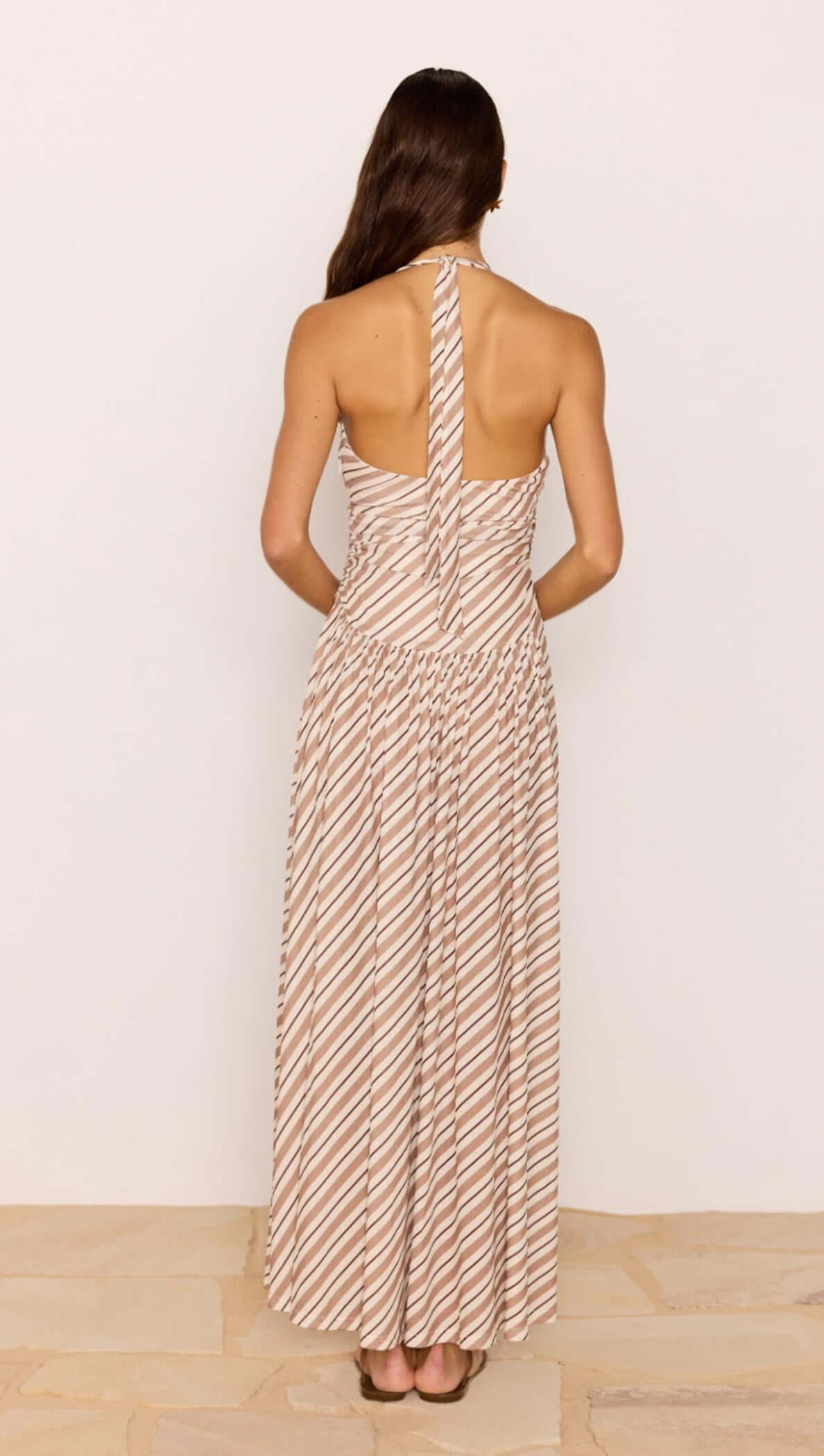 Back view of Brown &amp; Cream Stripe Low-Waist Halter Maxi Dress showcasing its elegant design and flowy skirt.